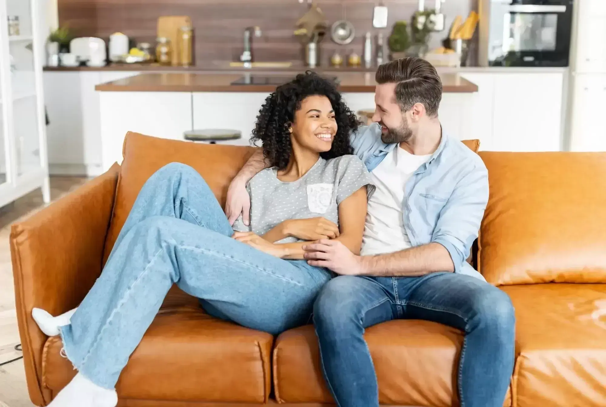 Couple Sitting On A Couch, Smiling At Each Other