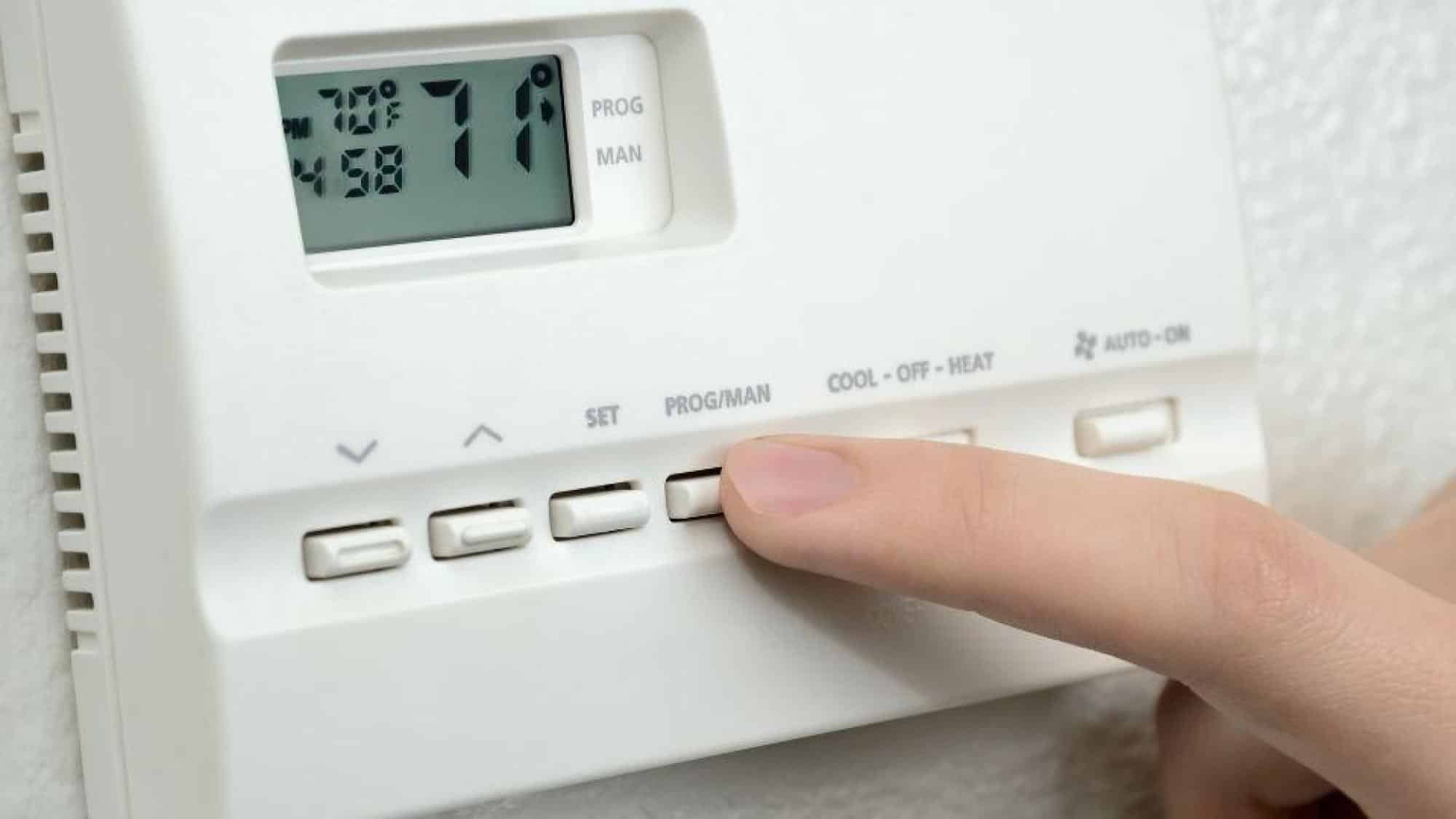 Person adjusting thermostat to set air conditioning for energy efficiency